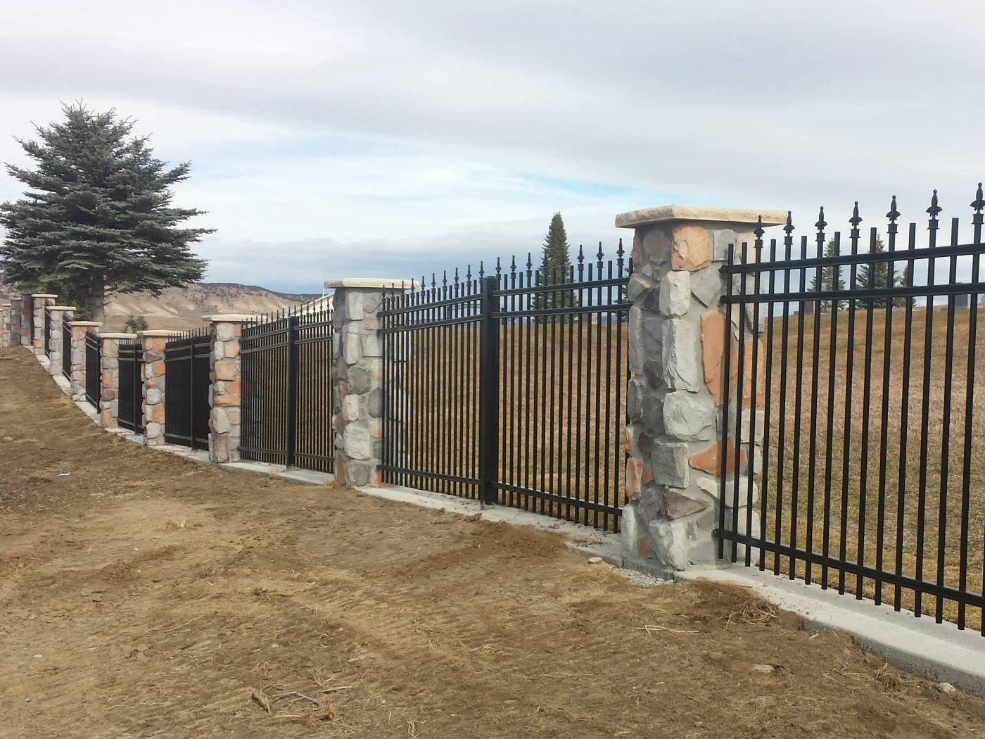 Photo of decorative residential fence made of aluminum with stone pillars.
